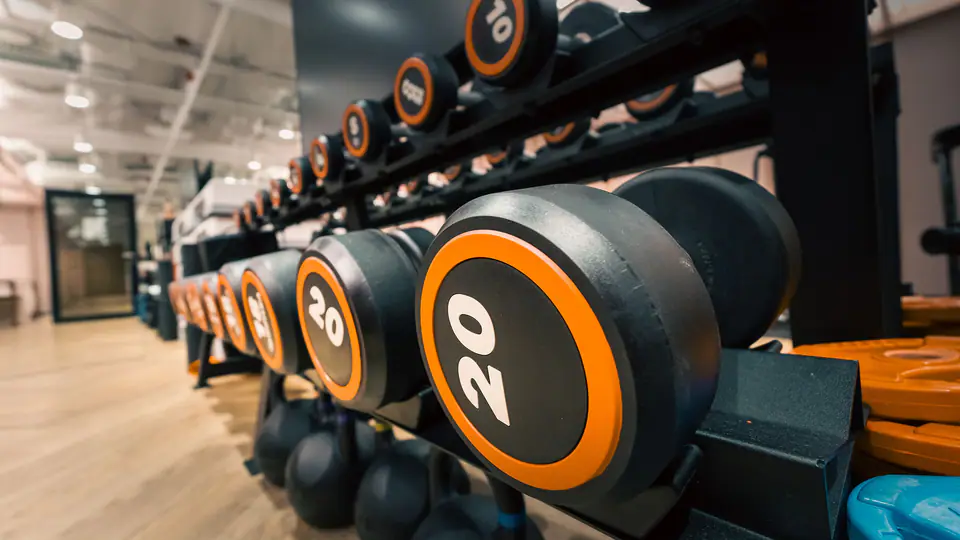 Rack of numbered dumbbells with orange trim above a row of kettlebells