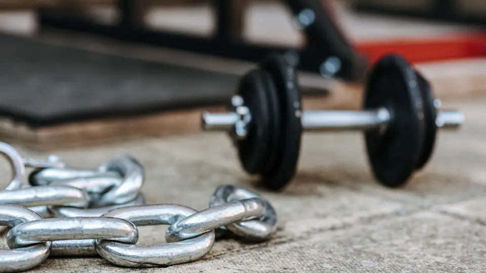 Plate-loaded dumbbell lying next to a heavy steel chain on a gym floor