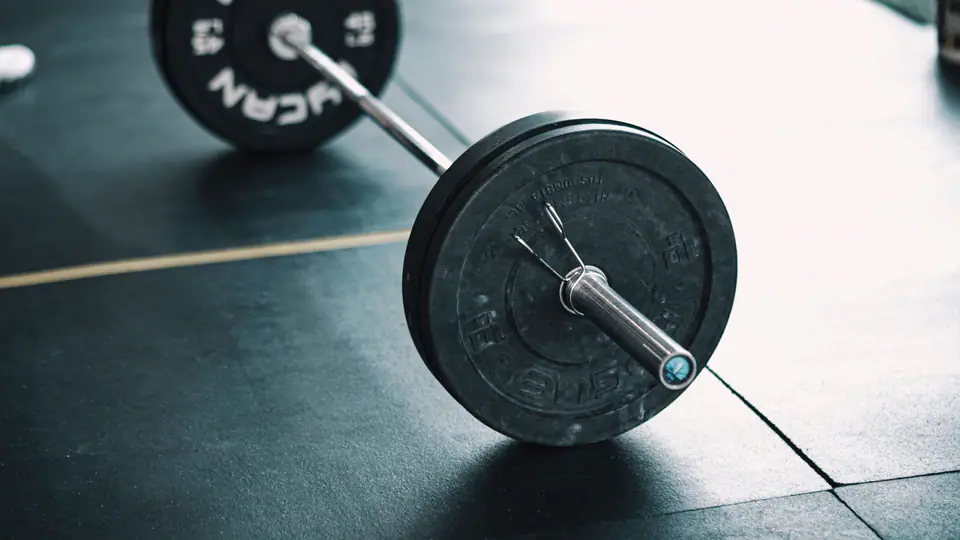 Barbell loaded with bumper plates resting on a gym floor, ready to be deadlifted