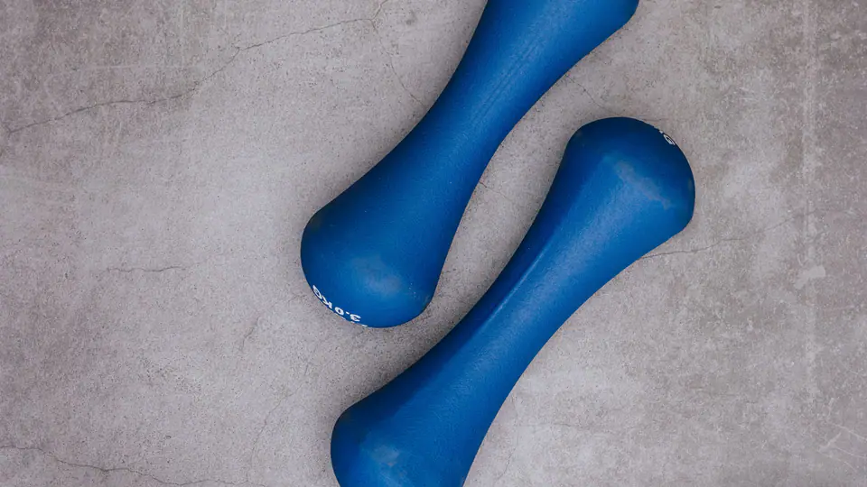 Flat lay of light blue dumbbells, a small weight plate, a jump rope and a water bottle on concrete
