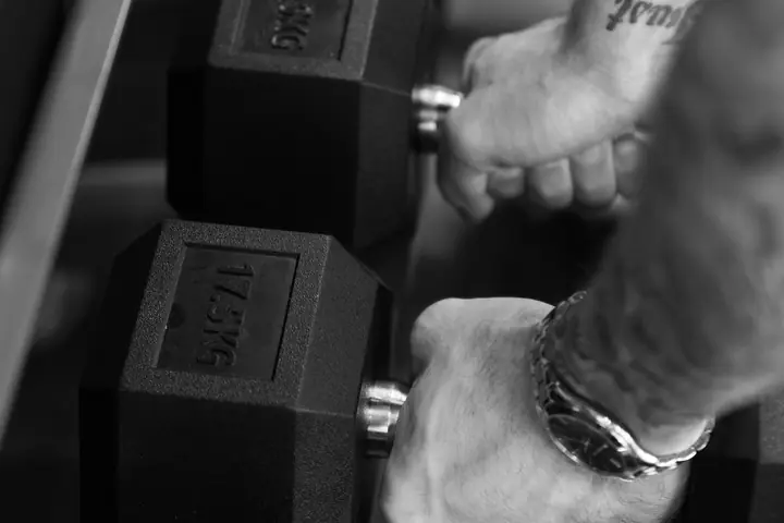Black-and-white photo of hands gripping hexagonal dumbbells on a rack
