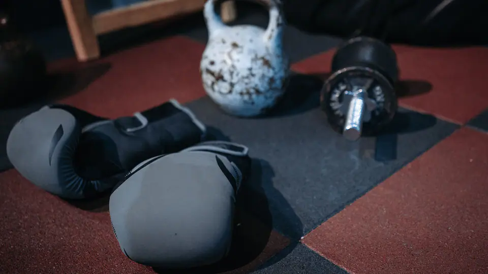 Kettlebell, boxing gloves and a dumbbell on a red and black gym floor