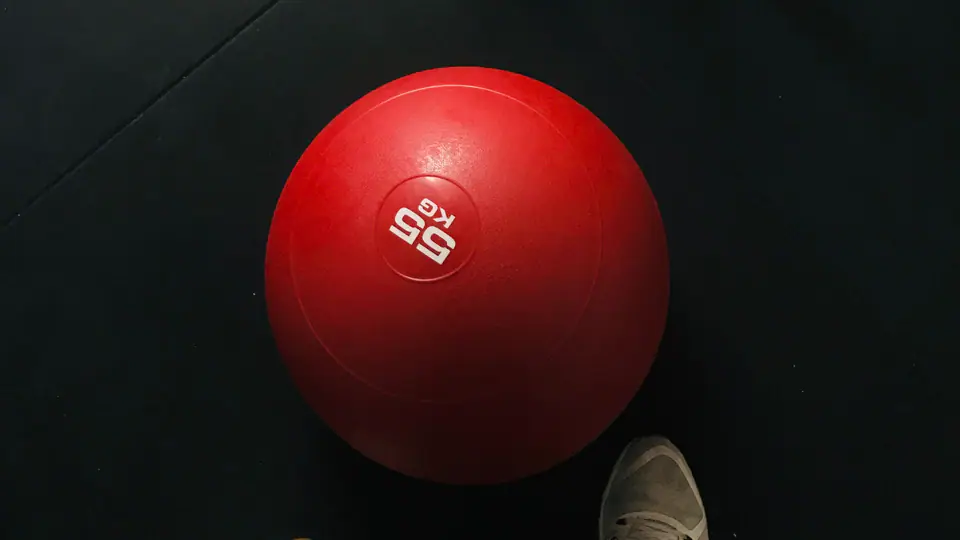 Top-down view of a barbell, a red slam ball and a pair of trainers on a gym floor