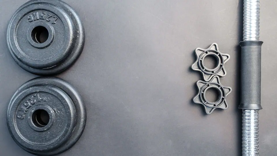 Two small iron plates, spin-lock collars and a dumbbell handle laid out on a grey surface