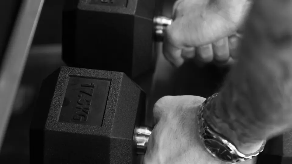 Black-and-white photo of hands gripping hexagonal dumbbells on a rack