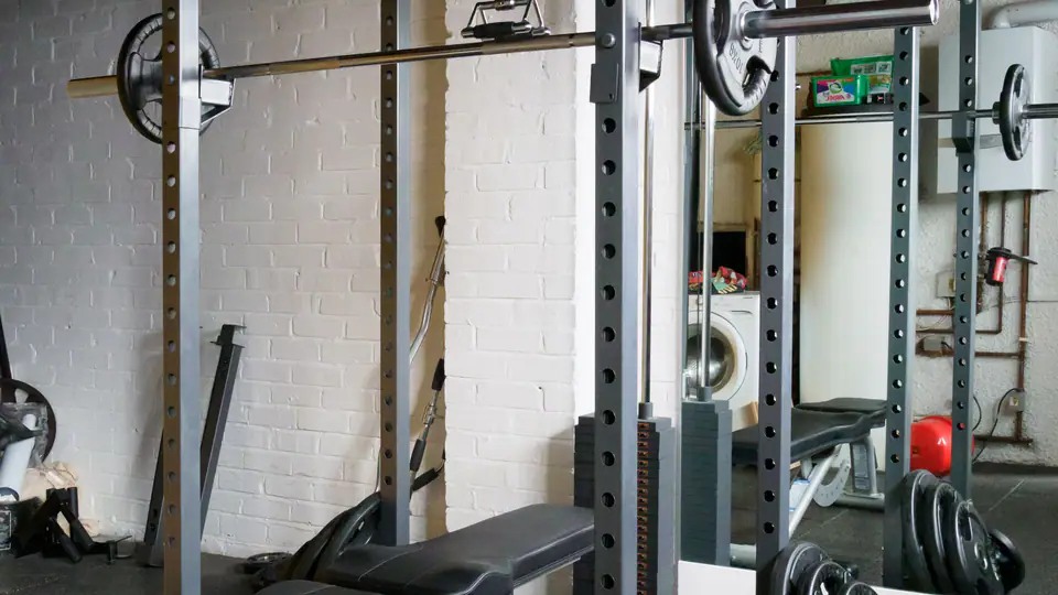 Power rack with a loaded barbell on the hooks and an adjustable bench inside