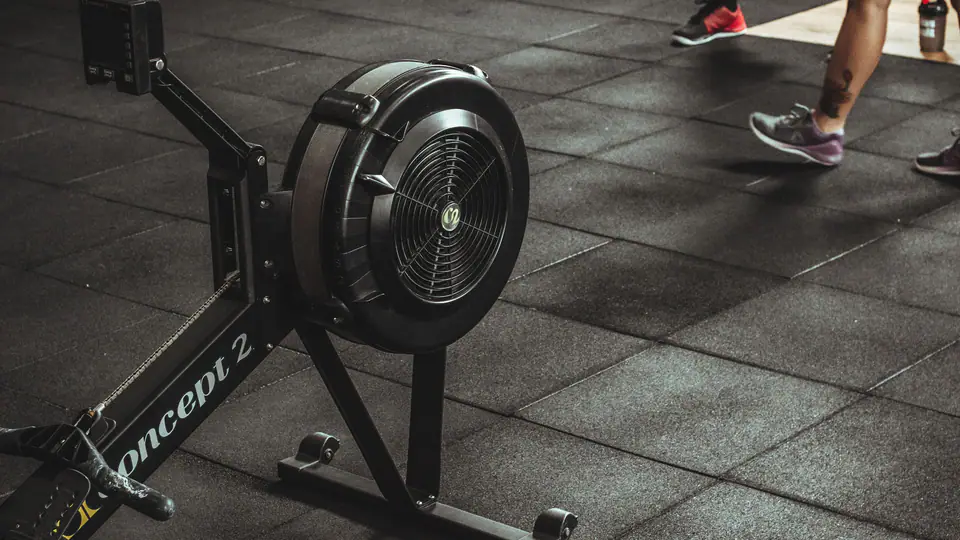 Air rowing machine on a rubber tile gym floor while people walk past