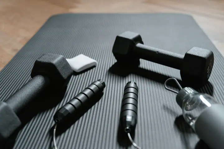 Exercise mat with two dumbbells, a jump rope and a water bottle