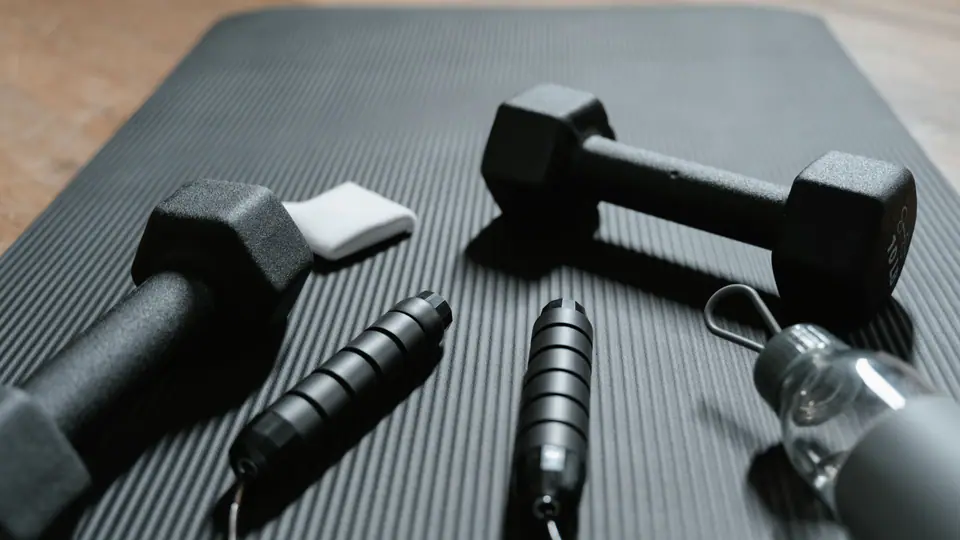 Exercise mat with two dumbbells, a jump rope and a water bottle
