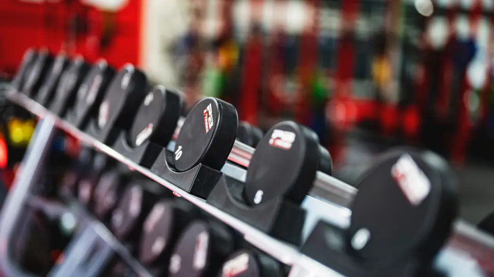 Long rack of round dumbbells in a busy gym, shot at an angle
