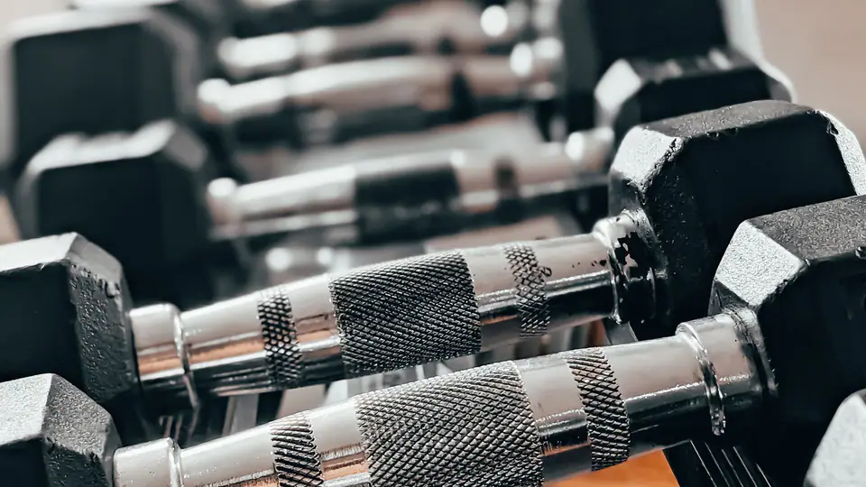 Hexagonal dumbbells with knurled handles on a rack in warm light