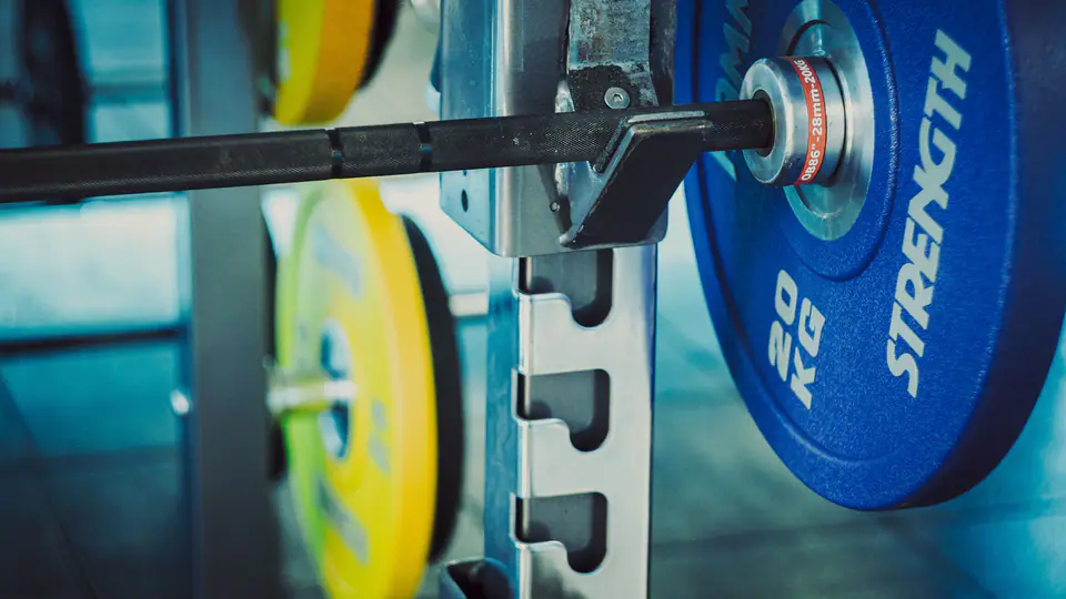 Loaded barbell sitting on rack hooks, with coloured plates stored behind