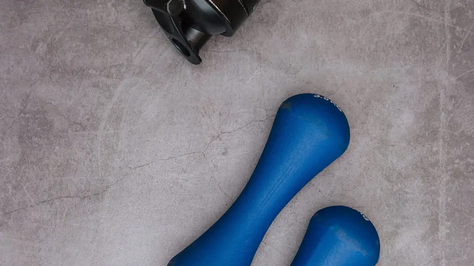 Flat lay of light blue dumbbells, a small weight plate, a jump rope and a water bottle on concrete