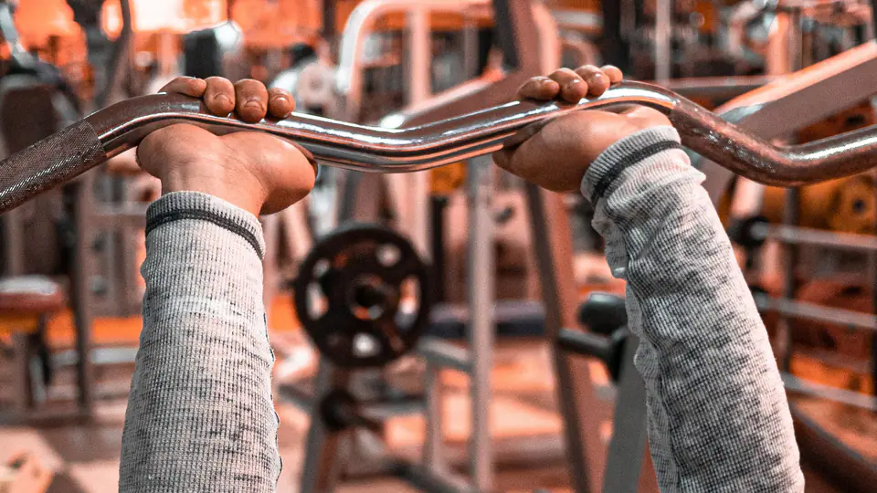 Lifter lying on a bench holding an EZ curl bar at arm’s length above his head