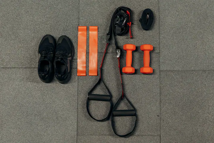 Flat lay of trainers, mini resistance bands, suspension straps and orange dumbbells