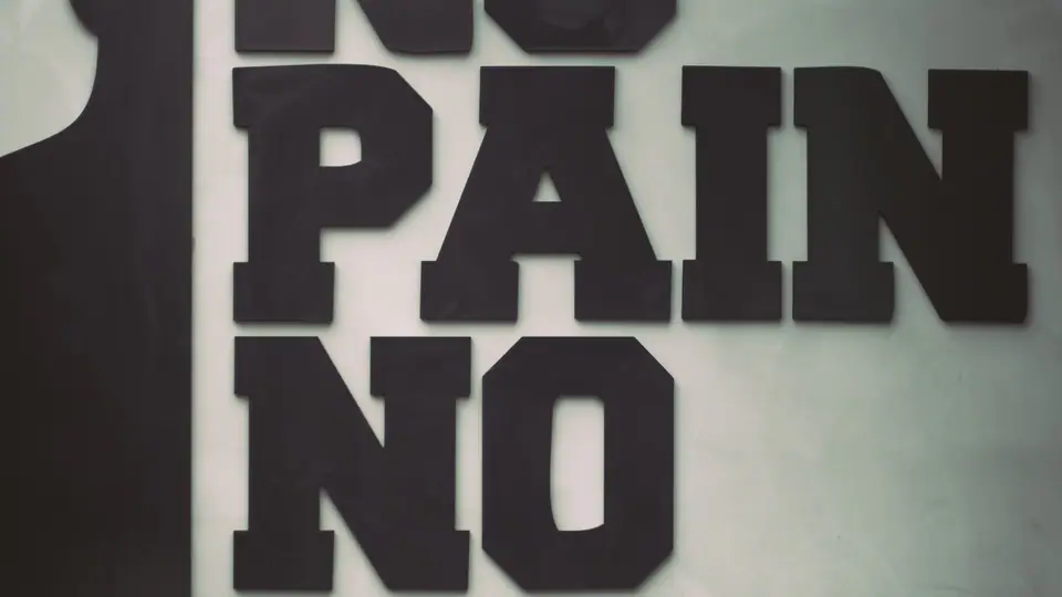 Gym wall painted with the words “No pain no gain” above a stability ball