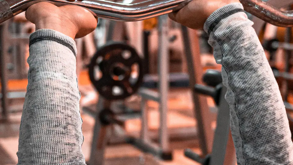 Lifter lying on a bench holding an EZ curl bar at arm’s length above his head