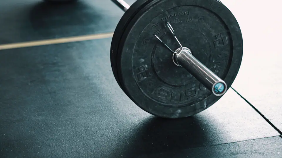 Barbell loaded with bumper plates resting on a gym floor, ready to be deadlifted