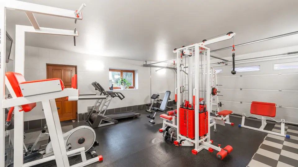 Home garage gym fitted with cable stations, a leg machine and a weight bench