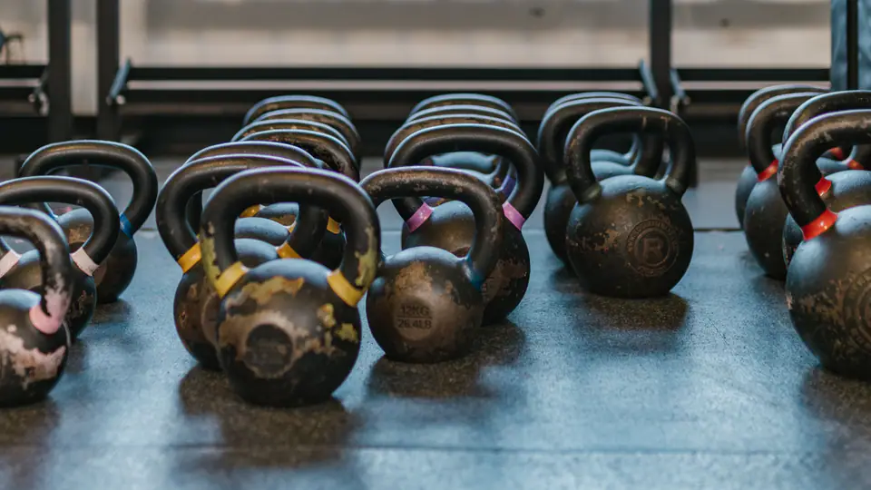Kettlebells on the floor in front of a dumbbell rack and a large window