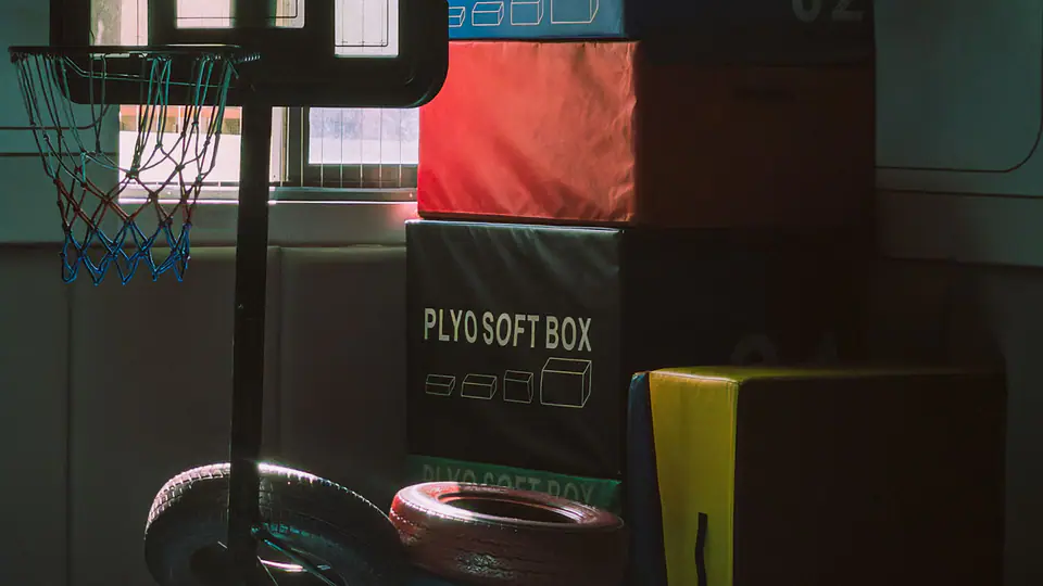 Soft plyometric boxes and a basketball hoop in a sunlit training room